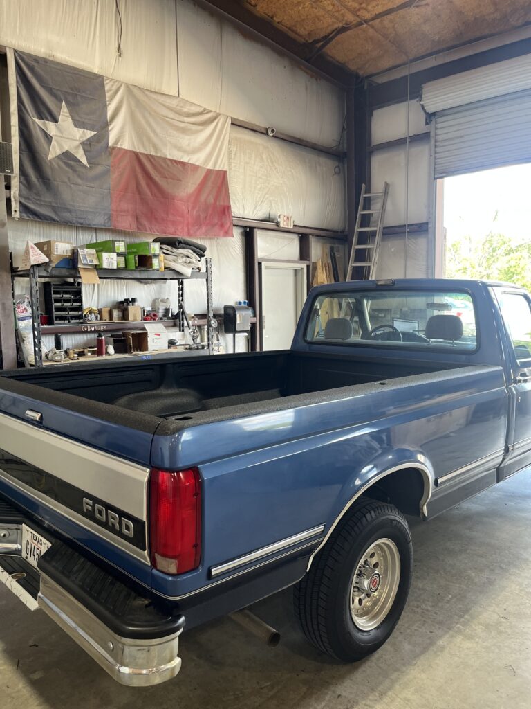 Classic blue Ford F-150 with a custom over-the-rail spray-in bed liner for maximum edge protection at Texas Truck Riggins in Bryan, TX.