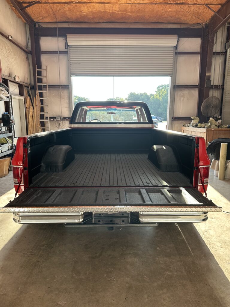 Professional spray-in bed liner installation on a red Ford pickup truck at Texas Truck Riggins in Bryan, TX.