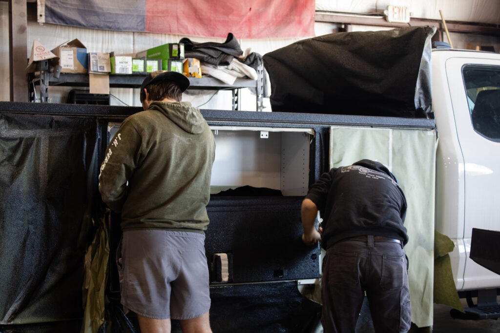 Texas Truck Riggins technicians removing protective paper from a freshly sprayed white service body to reveal a professional finish in Bryan, TX.